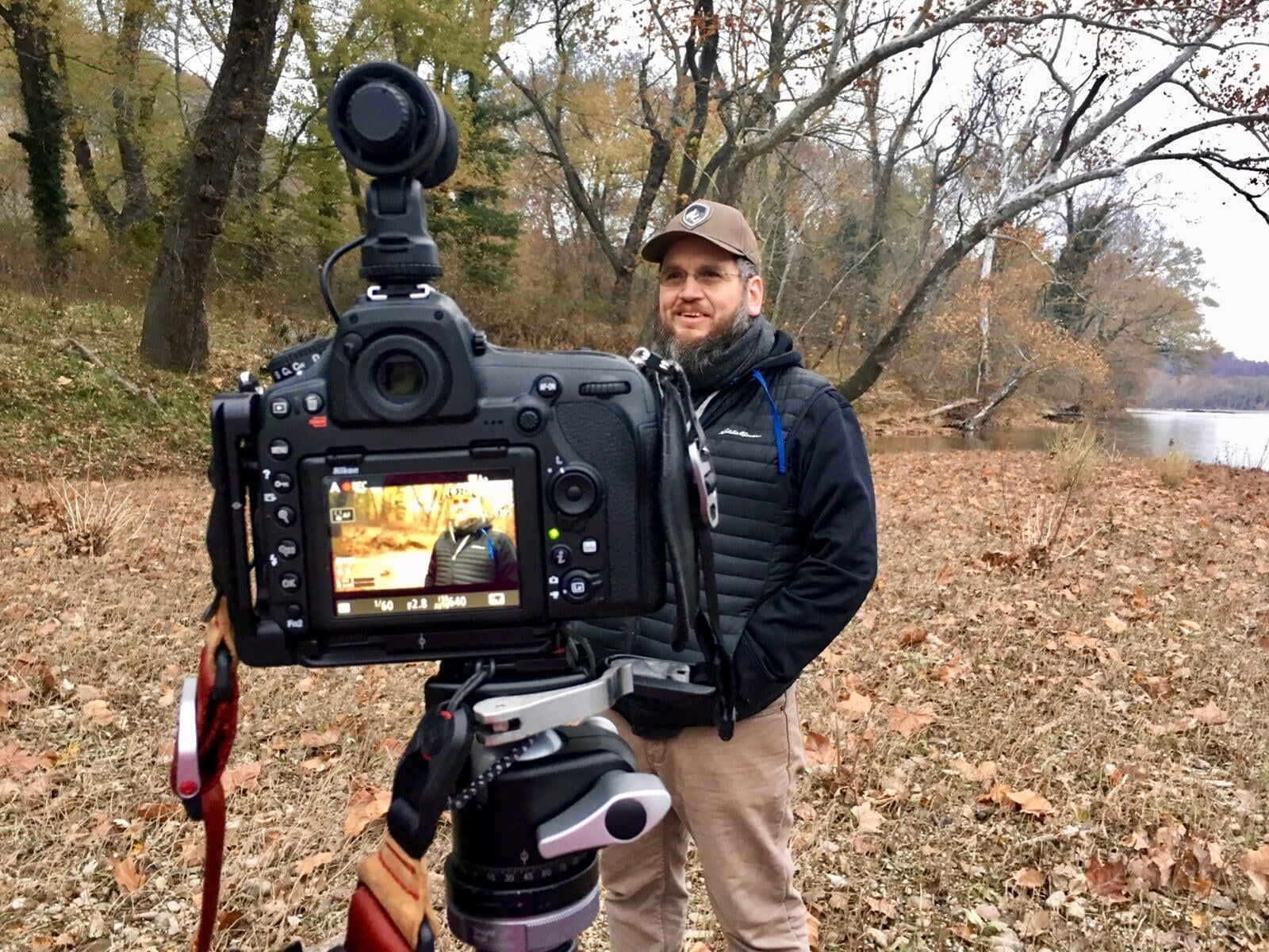 Photo of John Canan on camera giving an interview along the Potomac River